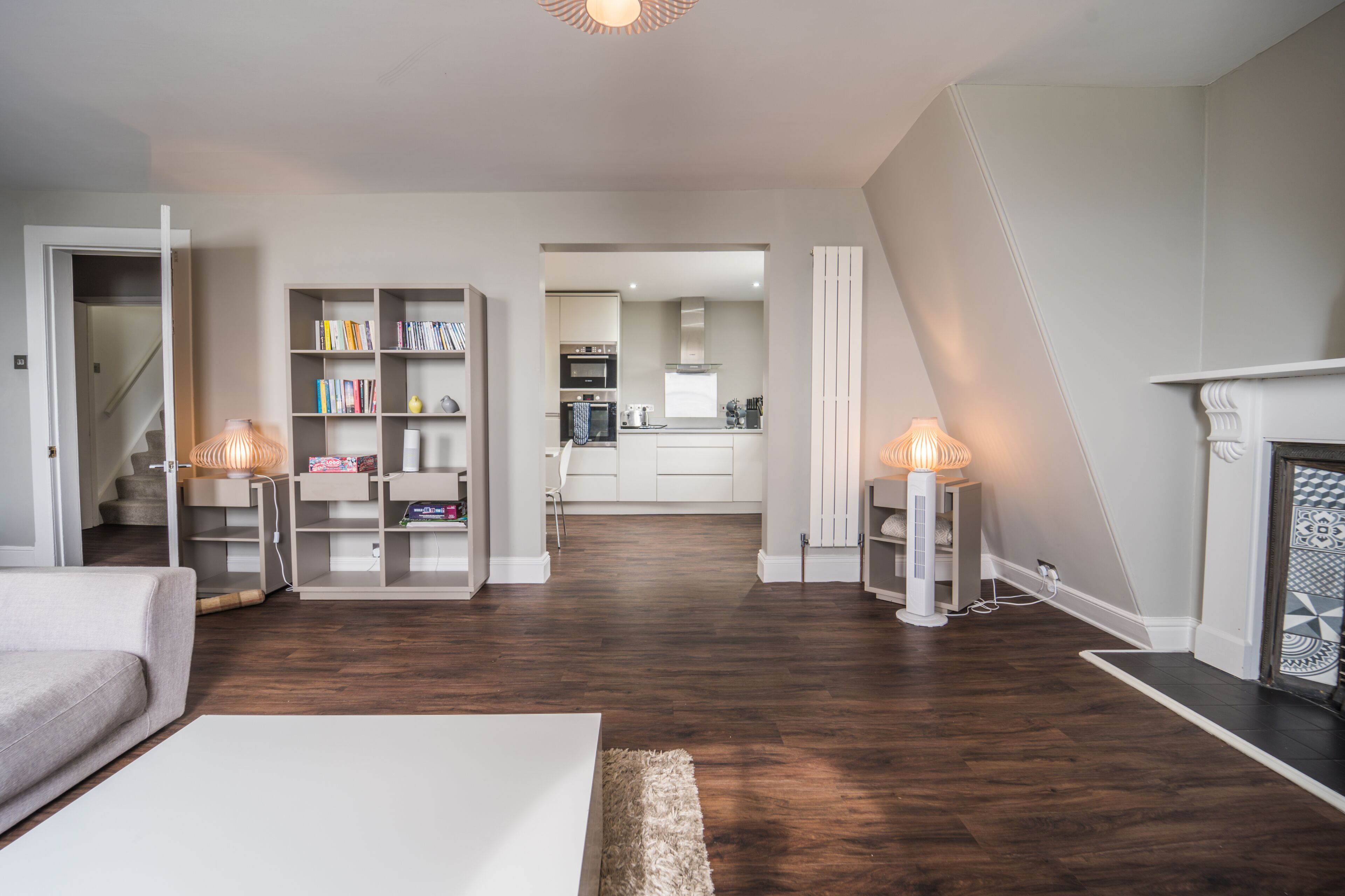 Uma sala de estar moderna com lareira, uma escada que leva a uma cozinha e uma estante de livros.