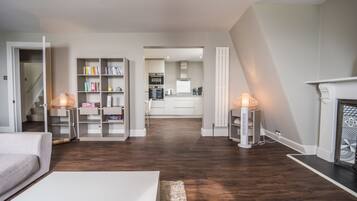 Uma sala de estar moderna com lareira, uma escada que leva a uma cozinha e uma estante de livros.