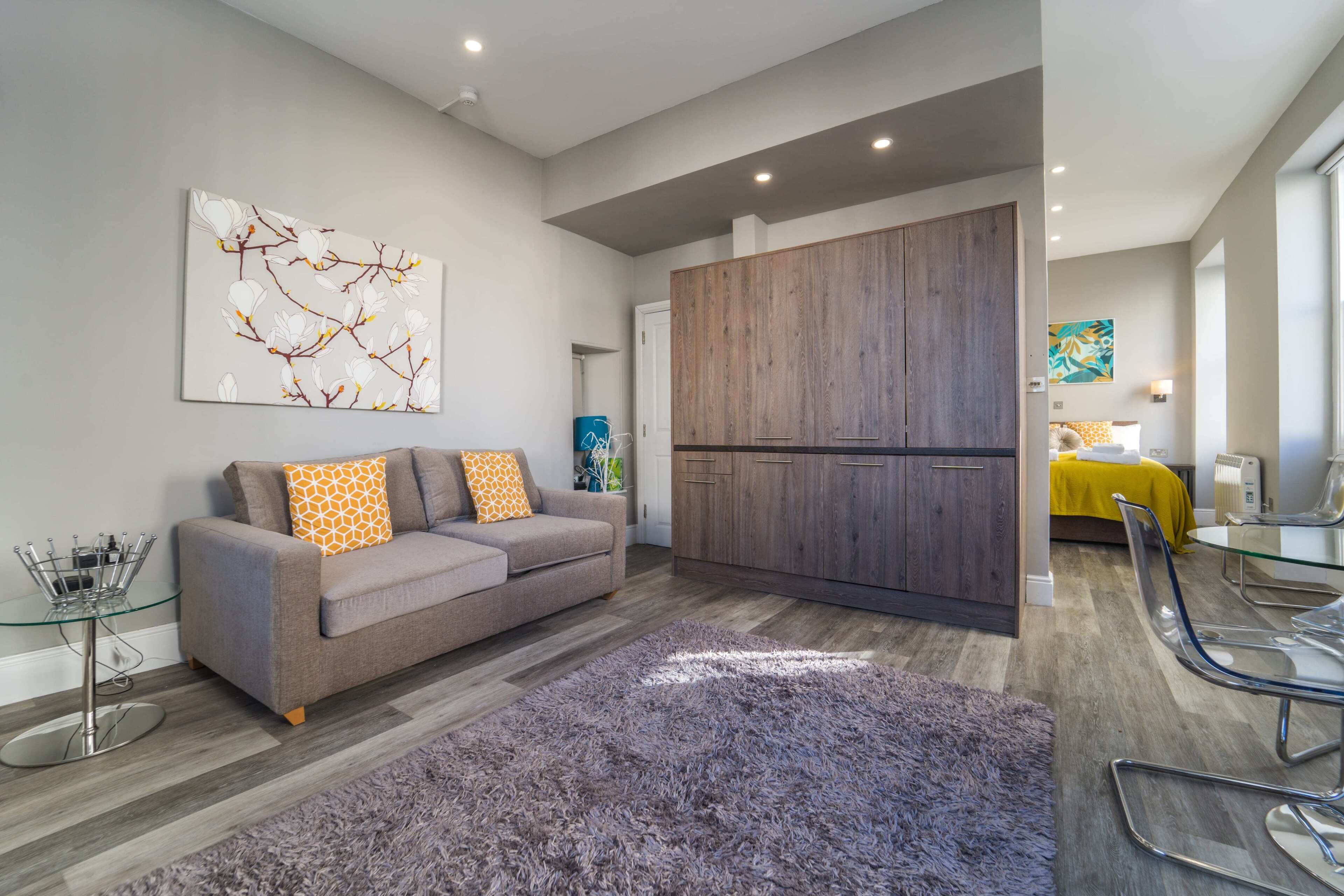 A modern living room with a grey sofa, a purple rug, and a wooden cabinet.