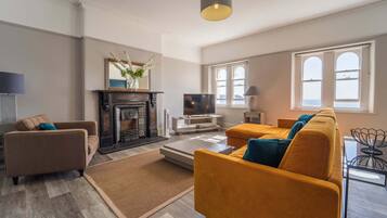 A modern living room with a fireplace, sofa, TV, and large windows.
