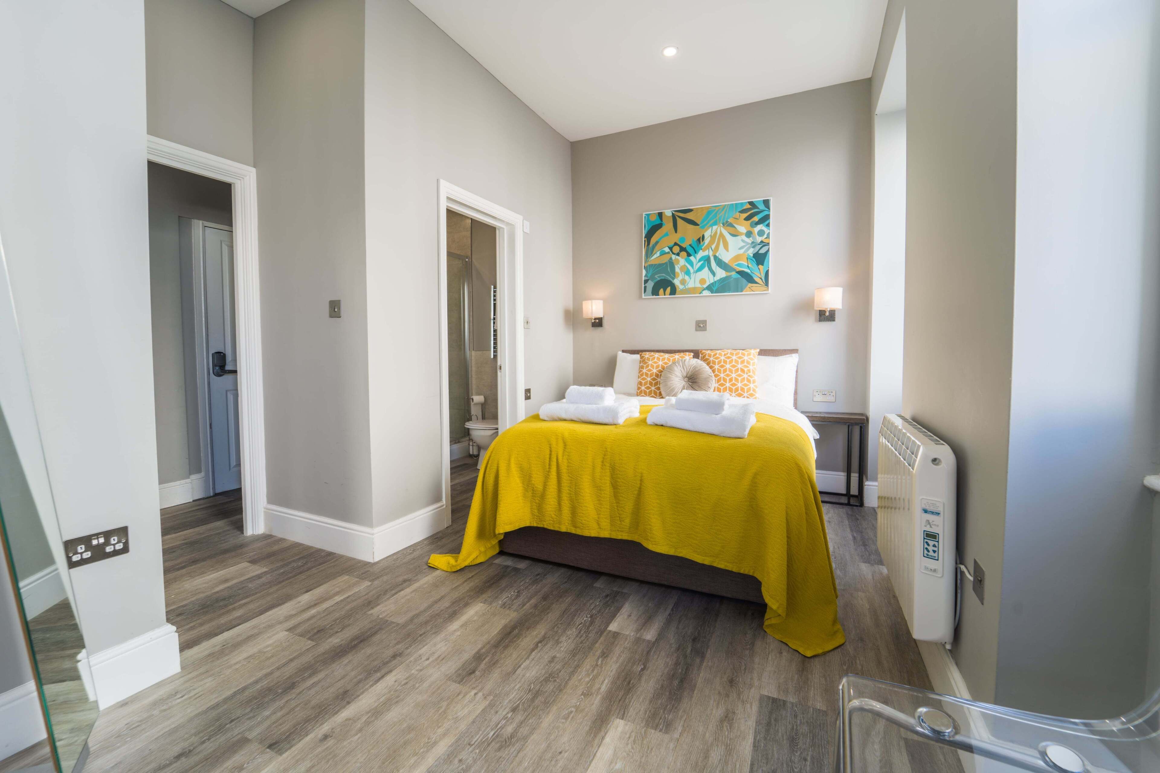 A hotel room with a bed, a radiator, a painting on the wall, and a door leading to another room.