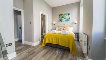 A hotel room with a bed, a radiator, a painting on the wall, and a door leading to another room.