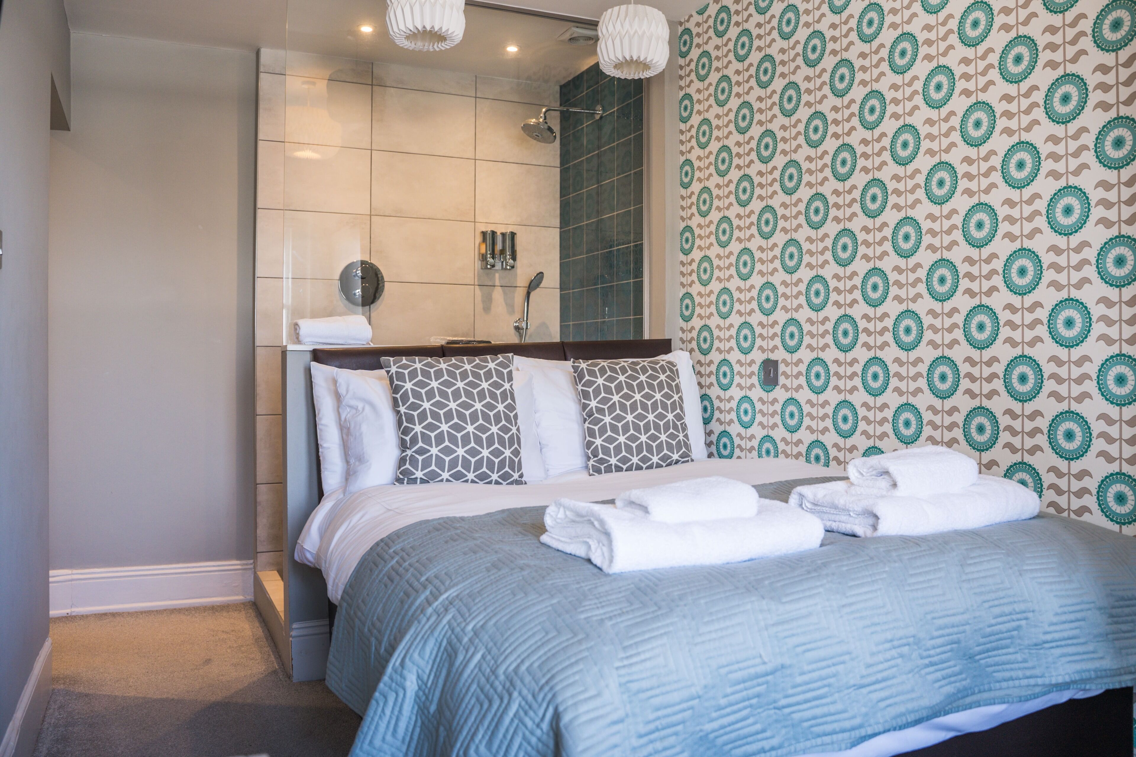 Une chambre d’hôtel avec un lit, un espace douche et un papier peint à motifs.
