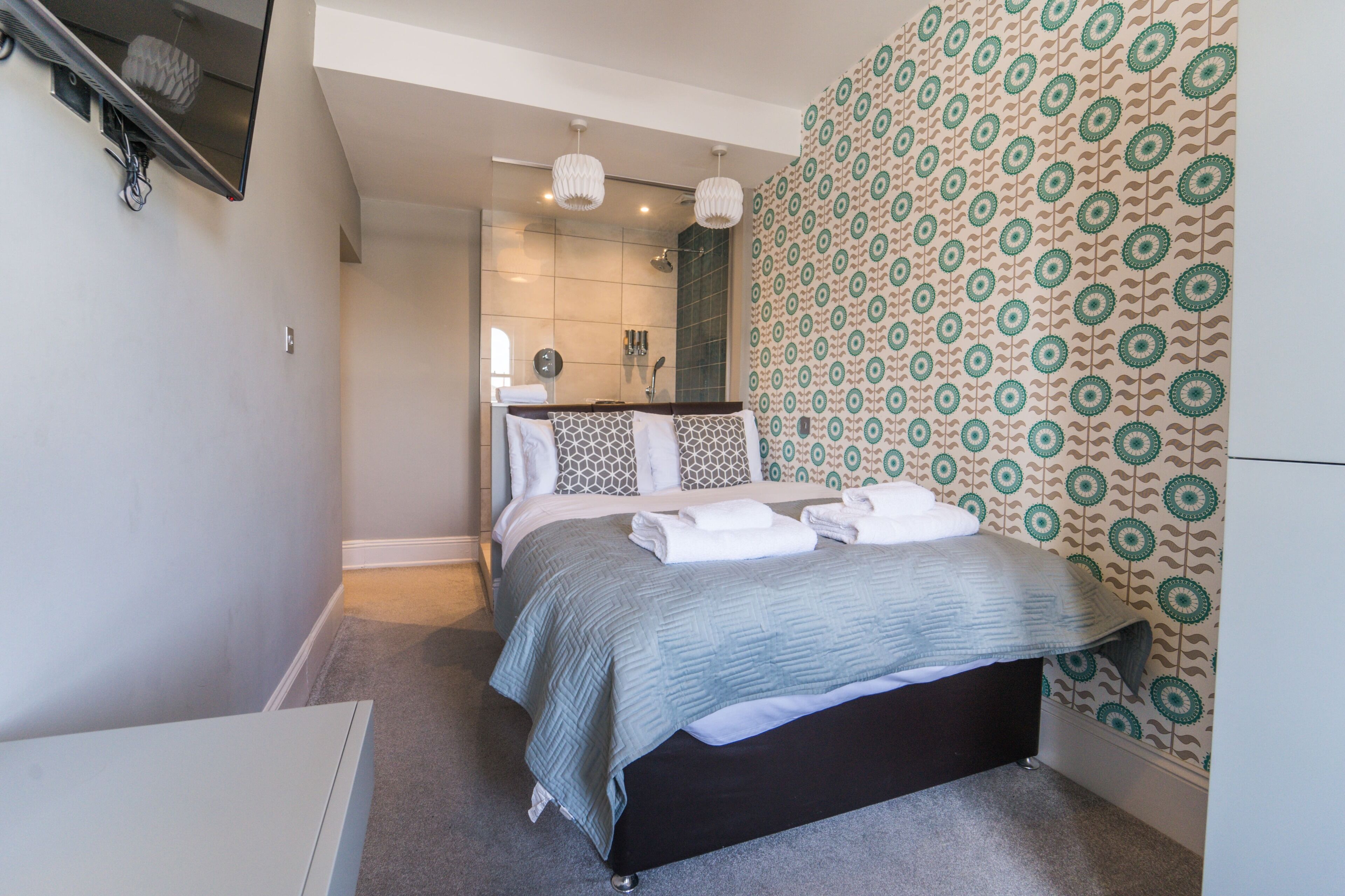 A modern bedroom with a bed, a shower area, and patterned wallpaper.