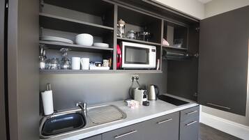 A modern kitchen with grey cabinets, a stainless steel sink, a microwave, and a kettle.