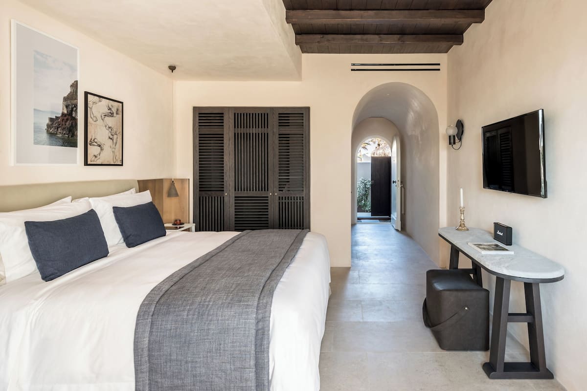 Un dormitorio con cama, mesita de noche, lámpara y televisor en la pared.