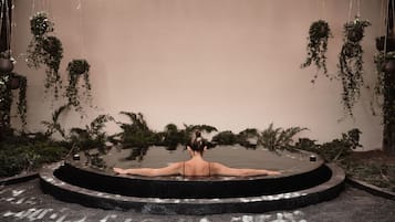 A circular hot tub with a person seated inside, surrounded by hanging plants.