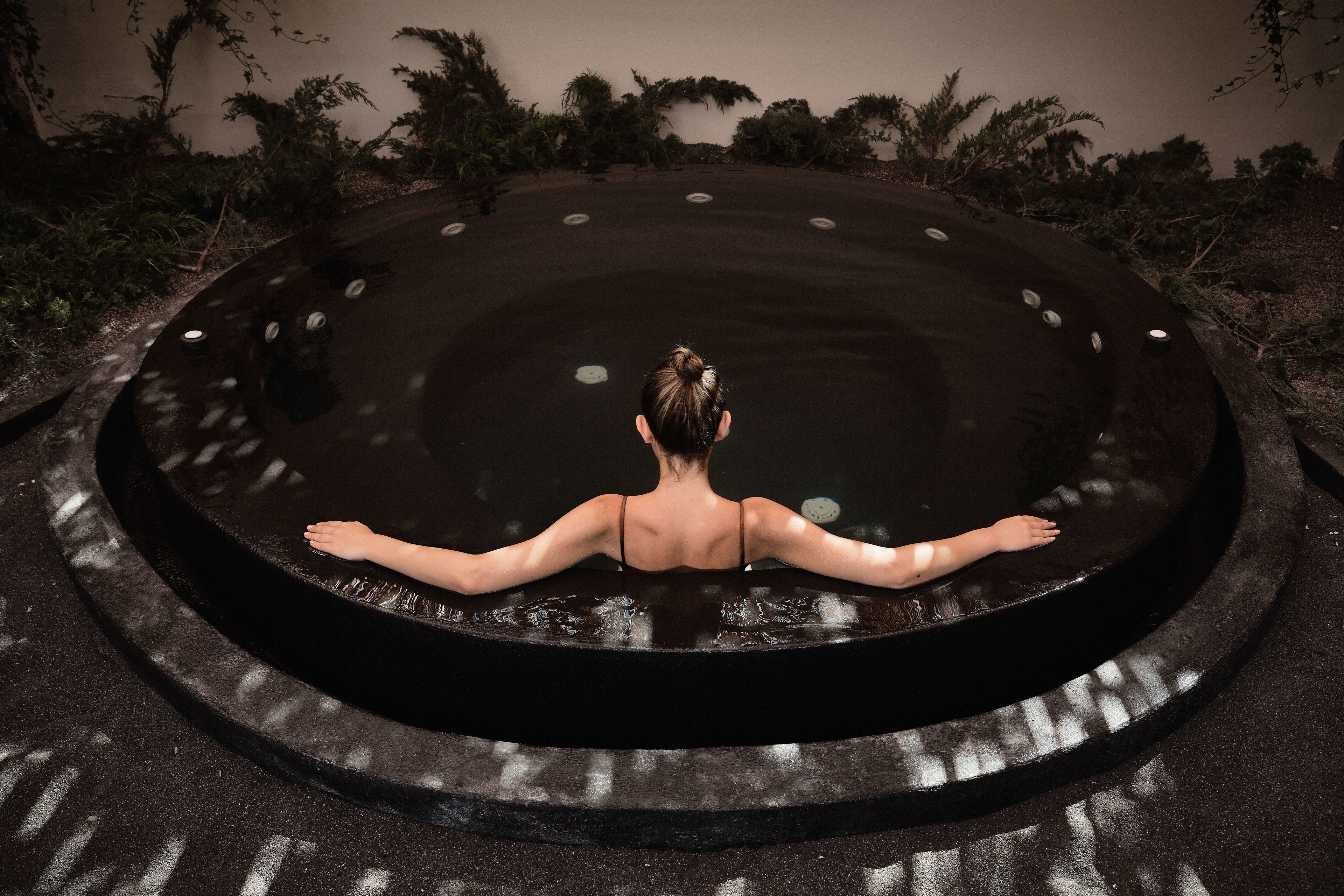 A person sitting in a circular water feature with a reflective surface, surrounded by greenery.