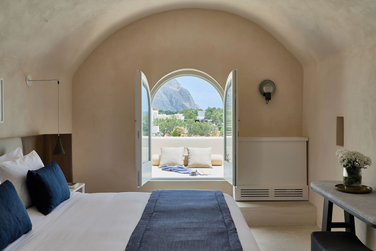 Un dormitorio con una cama grande, vistas a través de un arco abierto, una mesita de noche y otra mesita auxiliar.