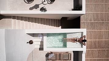 An aerial view of a modern hotel with a rooftop pool, lounge chairs, and a staircase.