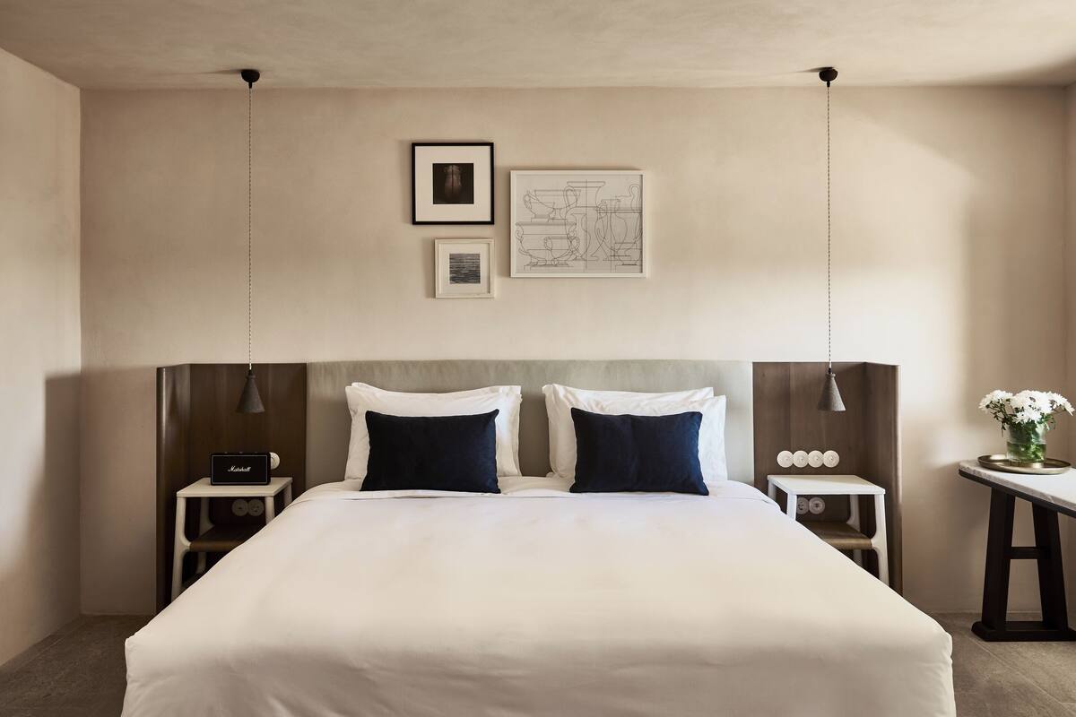 Una habitación de hotel impecable, con una cama grande, dos mesitas de noche y una pequeña mesa con un florero.