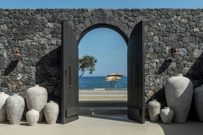 Un umbral abierto que da a una playa con paredes de piedra y grandes jarrones.
