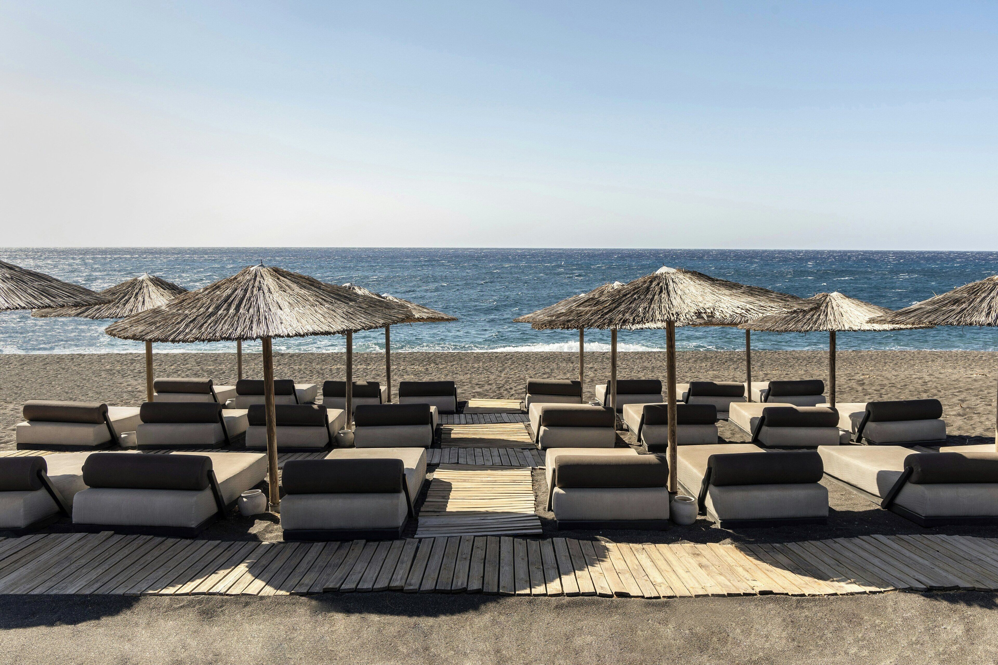 A beachside lounge area with sun loungers and thatched umbrellas, overlooking the sea.