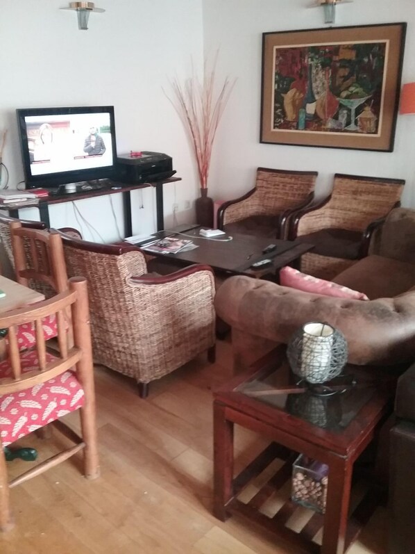Una sala de estar con sofá, sillas, una mesita de centro, televisor y un cuadro en la pared.