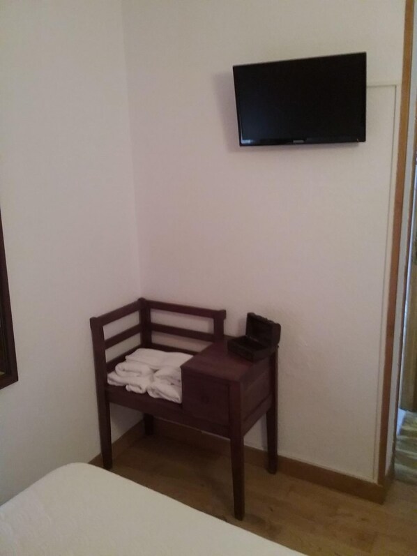 Una habitación pequeña con una cama de madera, una mesita de noche con lámpara y un televisor montado en la pared.