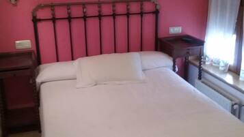 Un dormitorio con cabecera de metal, ropa de cama blanca, dos lámparas de noche y una ventana con cortinas.