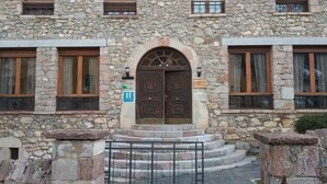 Un edificio de piedra con una entrada central en arco, varias ventanas con contraventanas de madera y un pequeño letrero que indica un hotel.