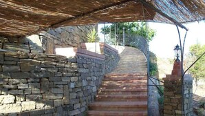 Una escalera de piedra que sube hacia una zona techada con barandilla de metal.
