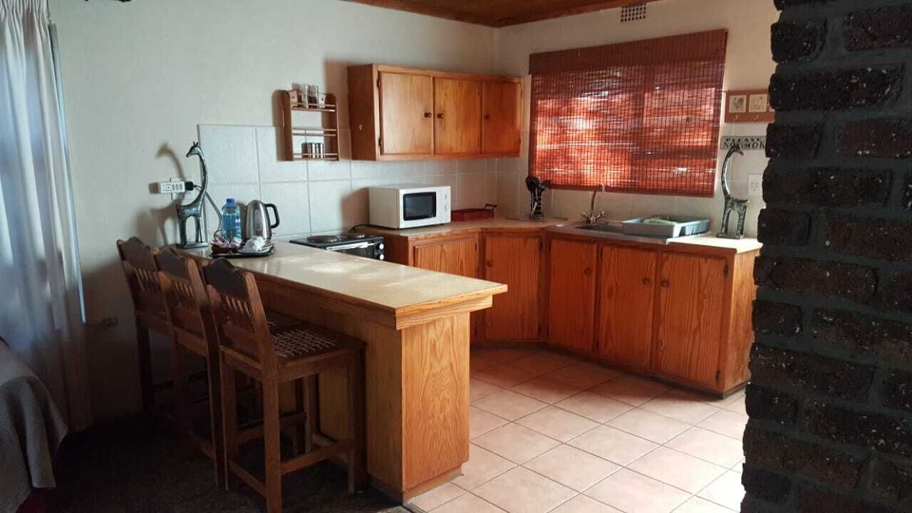 Una pequeña cocina con armarios de madera, microondas, pileta y barra con sillas.