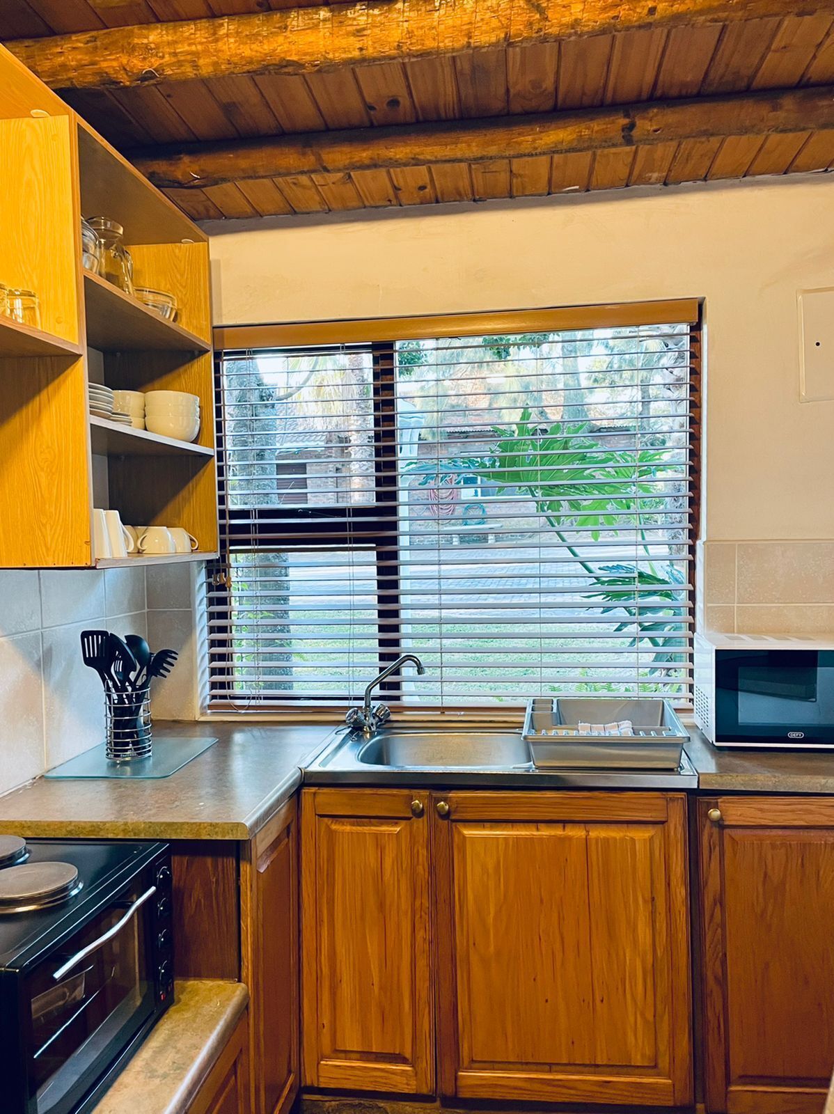 Cozinha com armários de madeira, forno embutido, micro-ondas e janela com persianas.