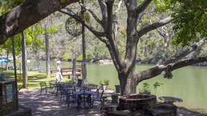 Une terrasse au bord de la rivière, avec des sièges d’extérieur, un foyer en pierre et une vue sur l’eau.