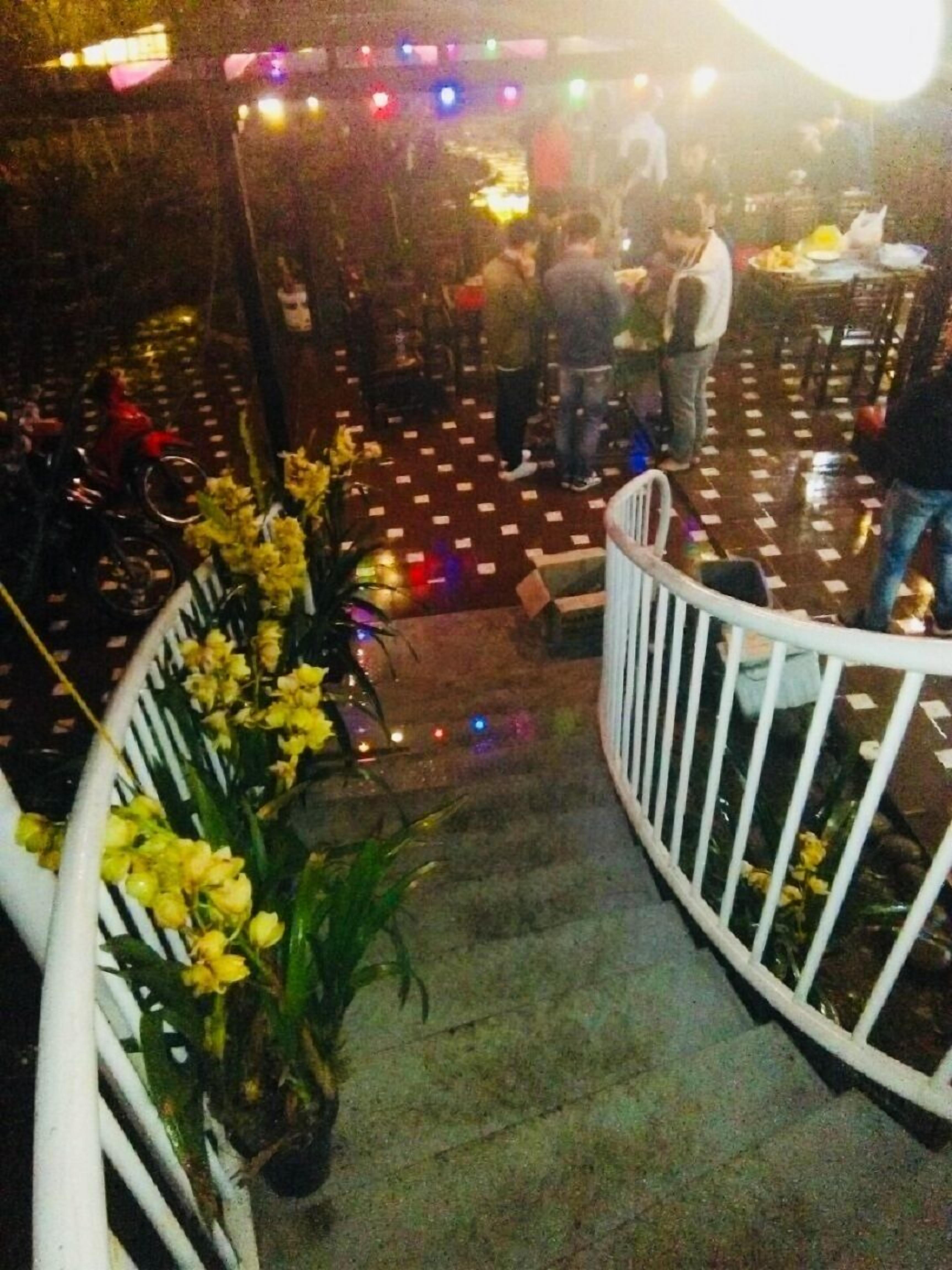 A staircase with a railing, surrounded by yellow flowers, leading to a seating area with tables and chairs.