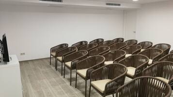 Un salón de conferencias con filas de sillas de mimbre y un escritorio blanco con un monitor de computadora.