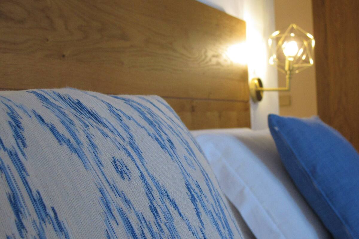 A bed with a white and blue striped pillow, a plain white pillow, and a blue pillow.