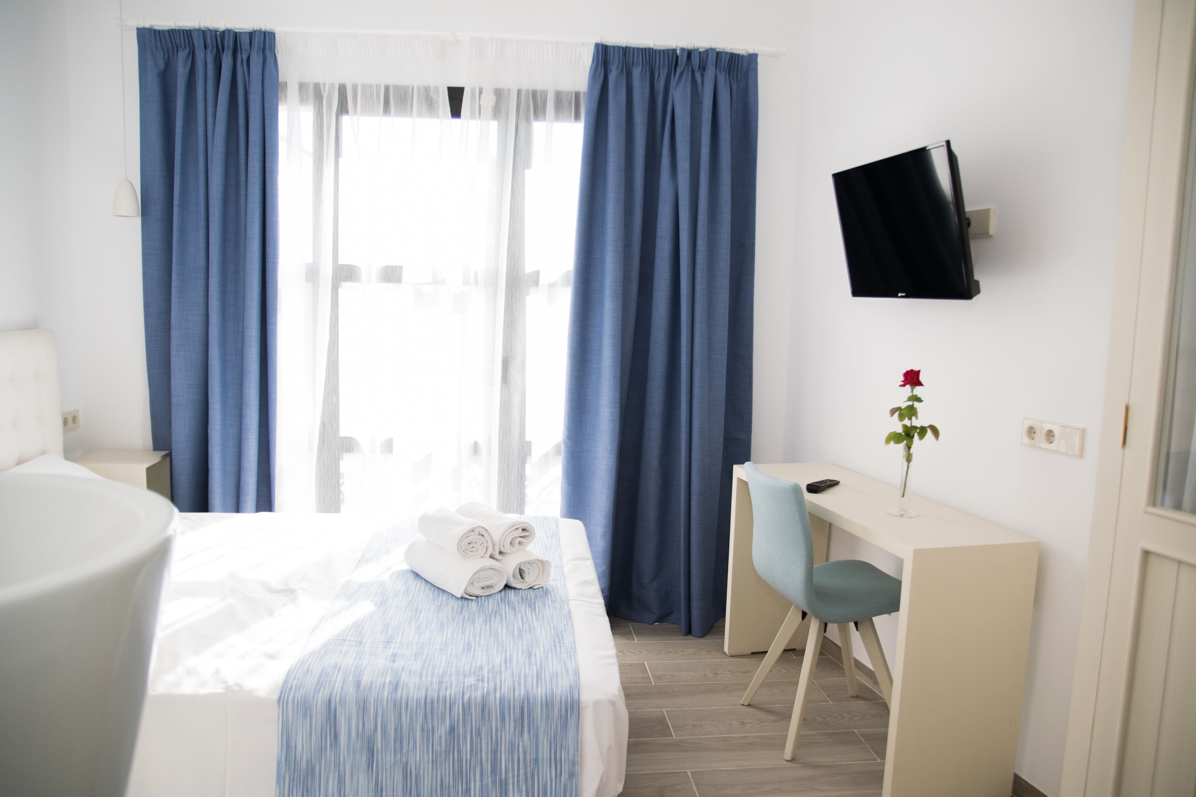 Una habitación de hotel con cama, escritorio, silla, televisor y ventana con cortinas.