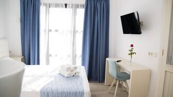 Una habitación de hotel con cama, escritorio, silla, televisor y ventana con cortinas.