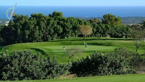 A golf course with a view of the ocean, surrounded by dense trees and greenery. - Petit Hotel Sant Miquel - Adults Only (Santanyi)