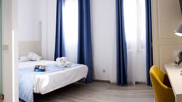 Habitación de hotel con un lavabo blanco, una cama con ropa de cama azul, un escritorio con lámpara y una silla.
