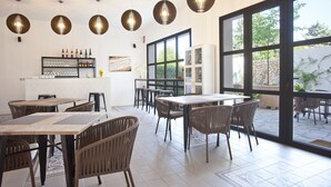 A restaurant with multiple tables and chairs, a bar area with bottles and glasses, and large windows offering a view of the outdoors. - Petit Hotel Sant Miquel - Adults Only (Santanyi)