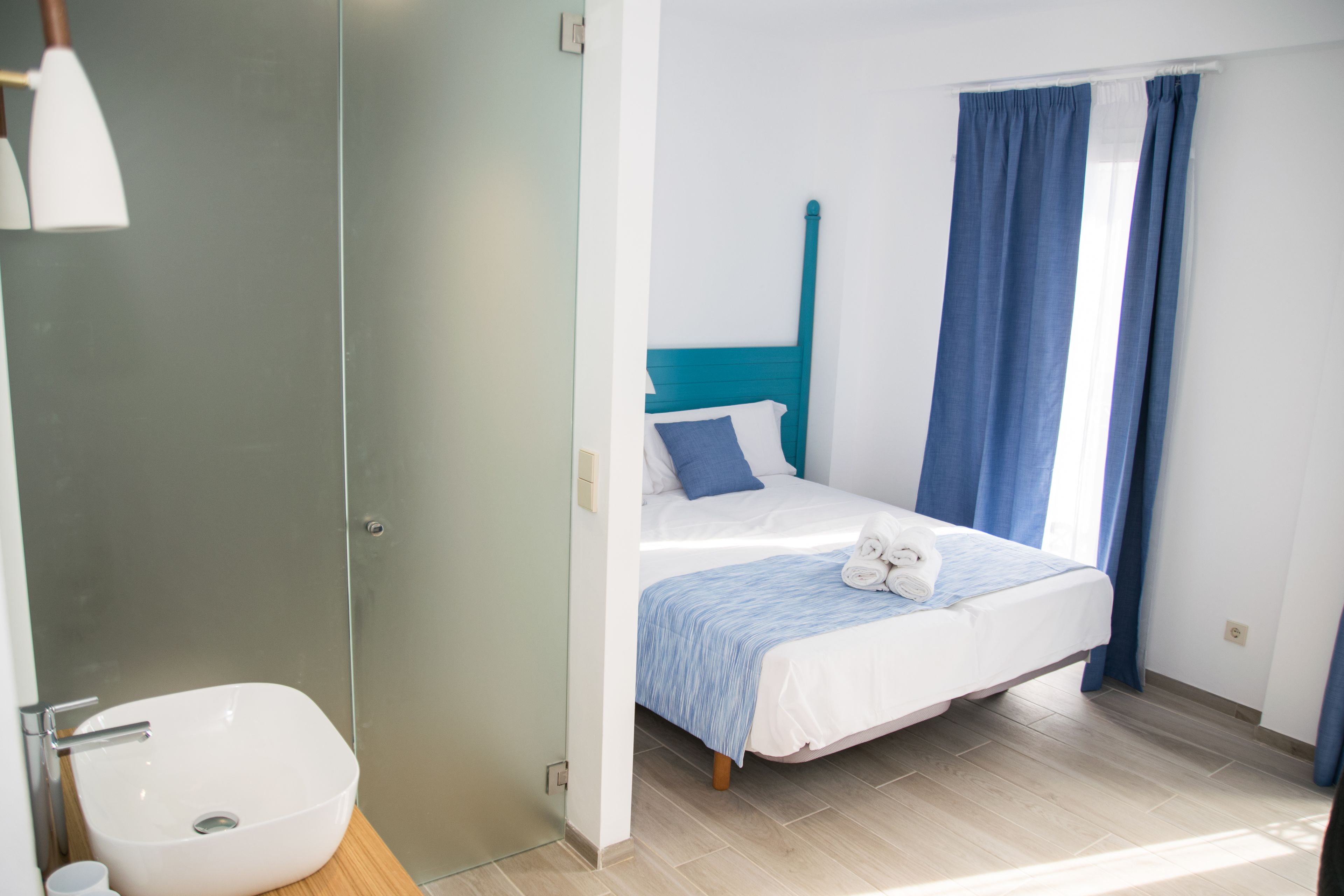A bedroom with a bed, a bedside table, a lamp, and a window with curtains.