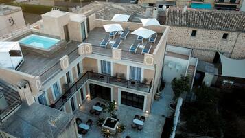 Un edificio de varios niveles con piscina en la azotea, zona de estar al aire libre y patio con mesas y sillas.
