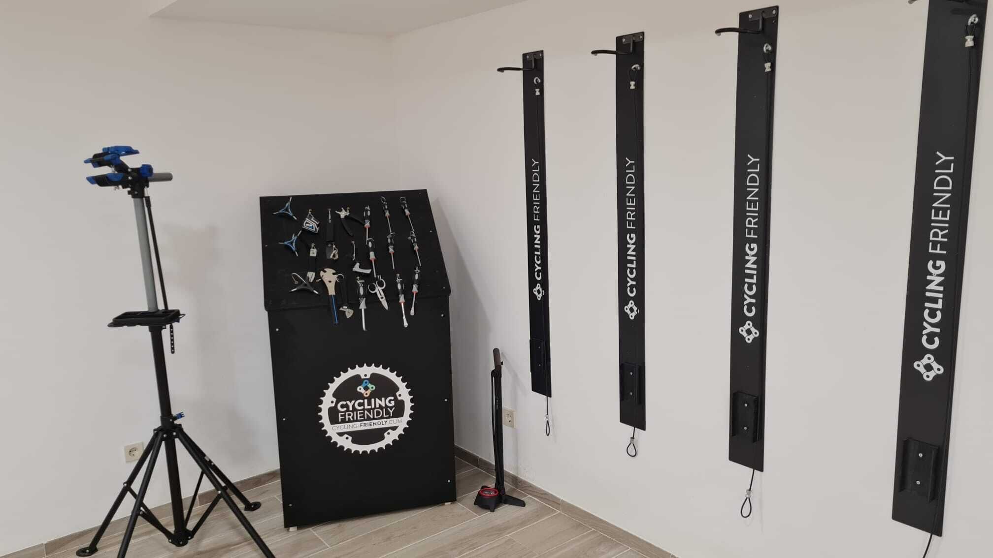 A room with a tripod-mounted camera, a black storage unit with cycling accessories, and multiple black banners on the wall.