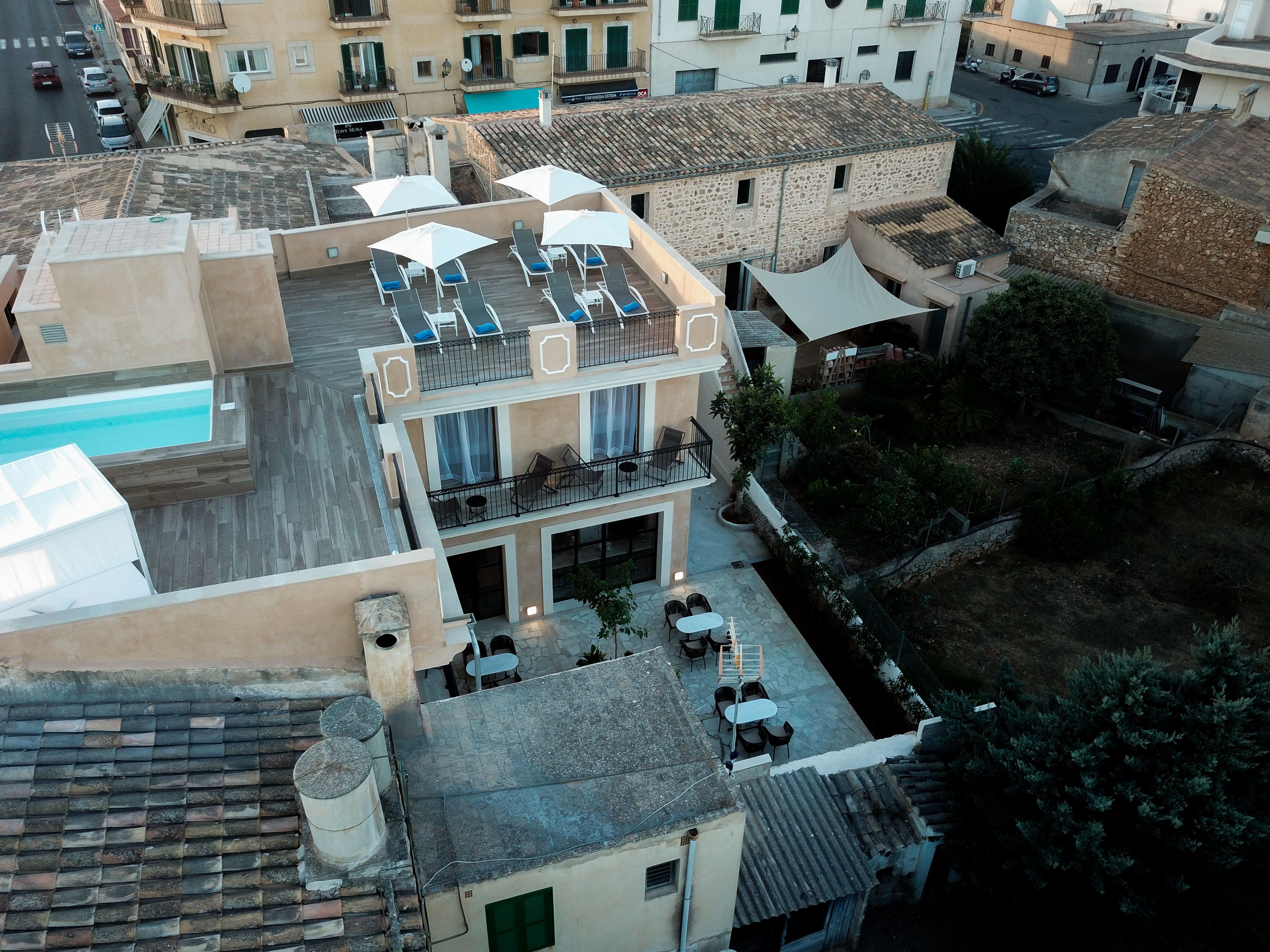 A rooftop terrace with sun loungers and umbrellas, a pool, and a view of the surrounding buildings.