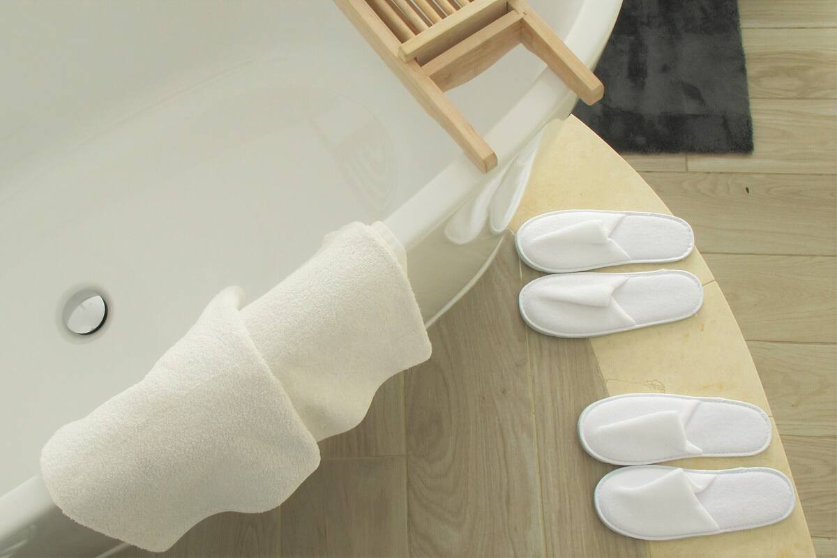 A bathtub with a white towel and slippers on the floor.