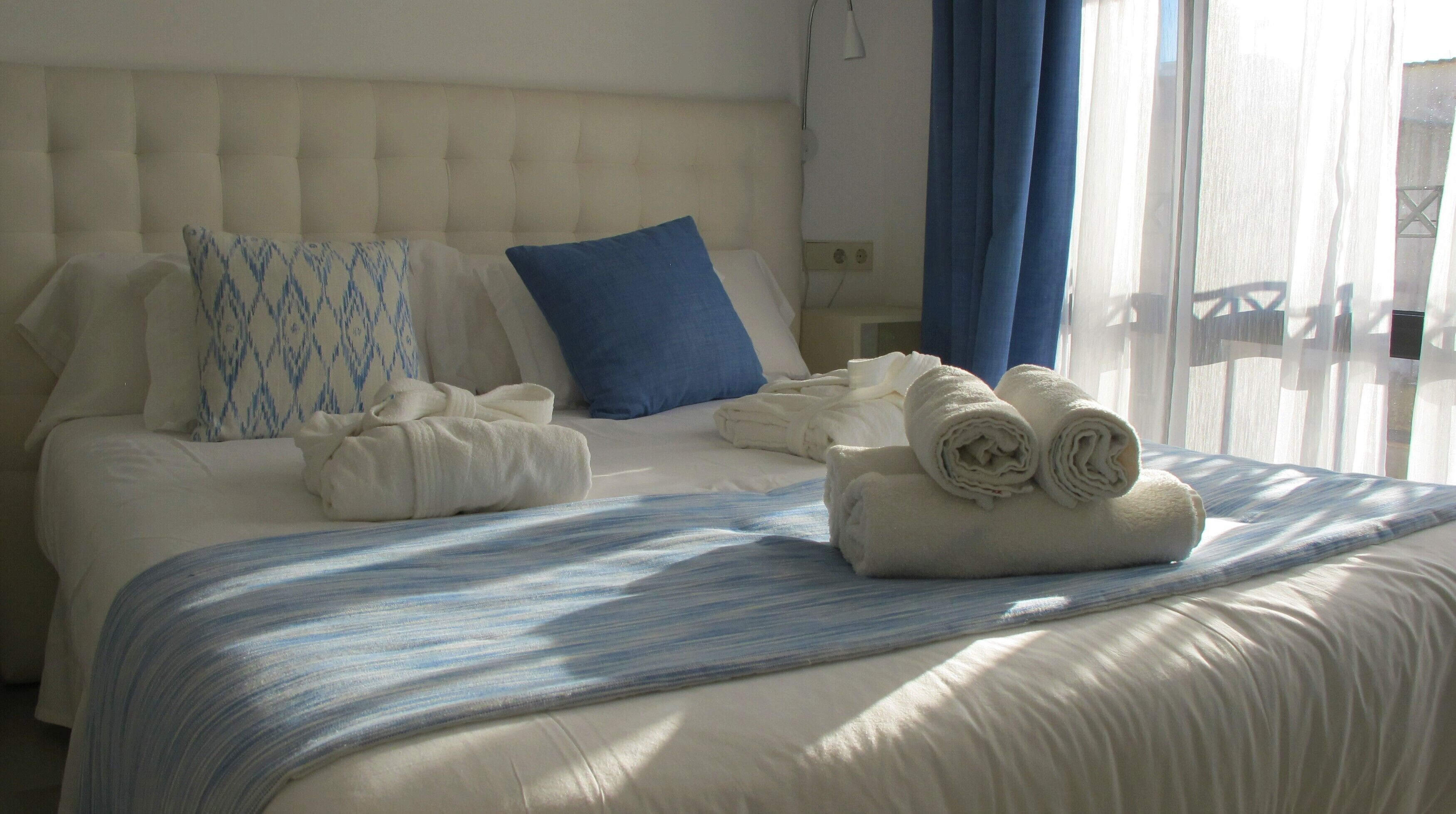 Ein ordentlich bezogenes Bett mit einem gestreiften Bettüberwurf, einem gepolsterten Kopfteil und einem blauen Kopfkissen.