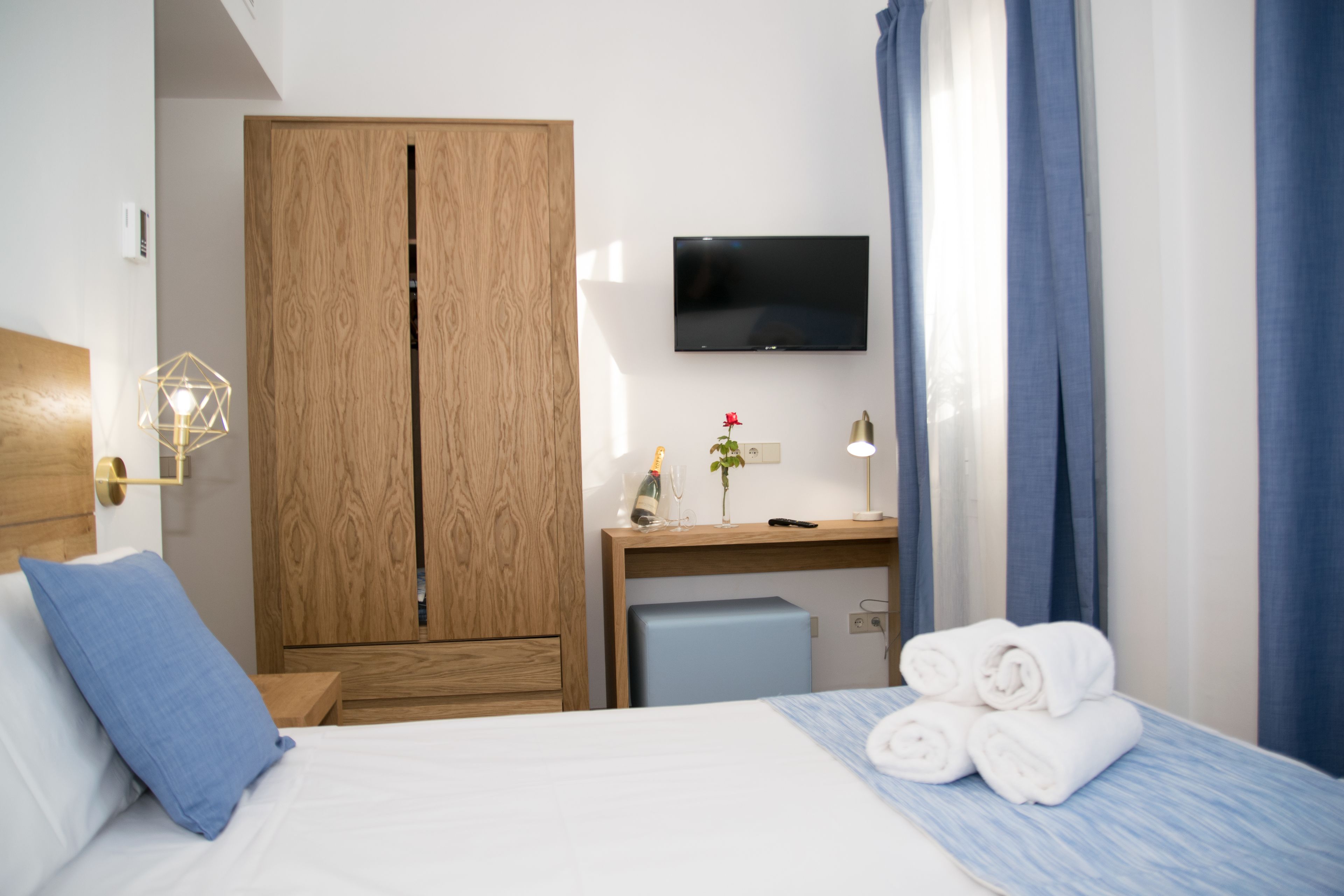 Una habitación de hotel con cama, escritorio, televisor, armario y un pequeño refrigerador.