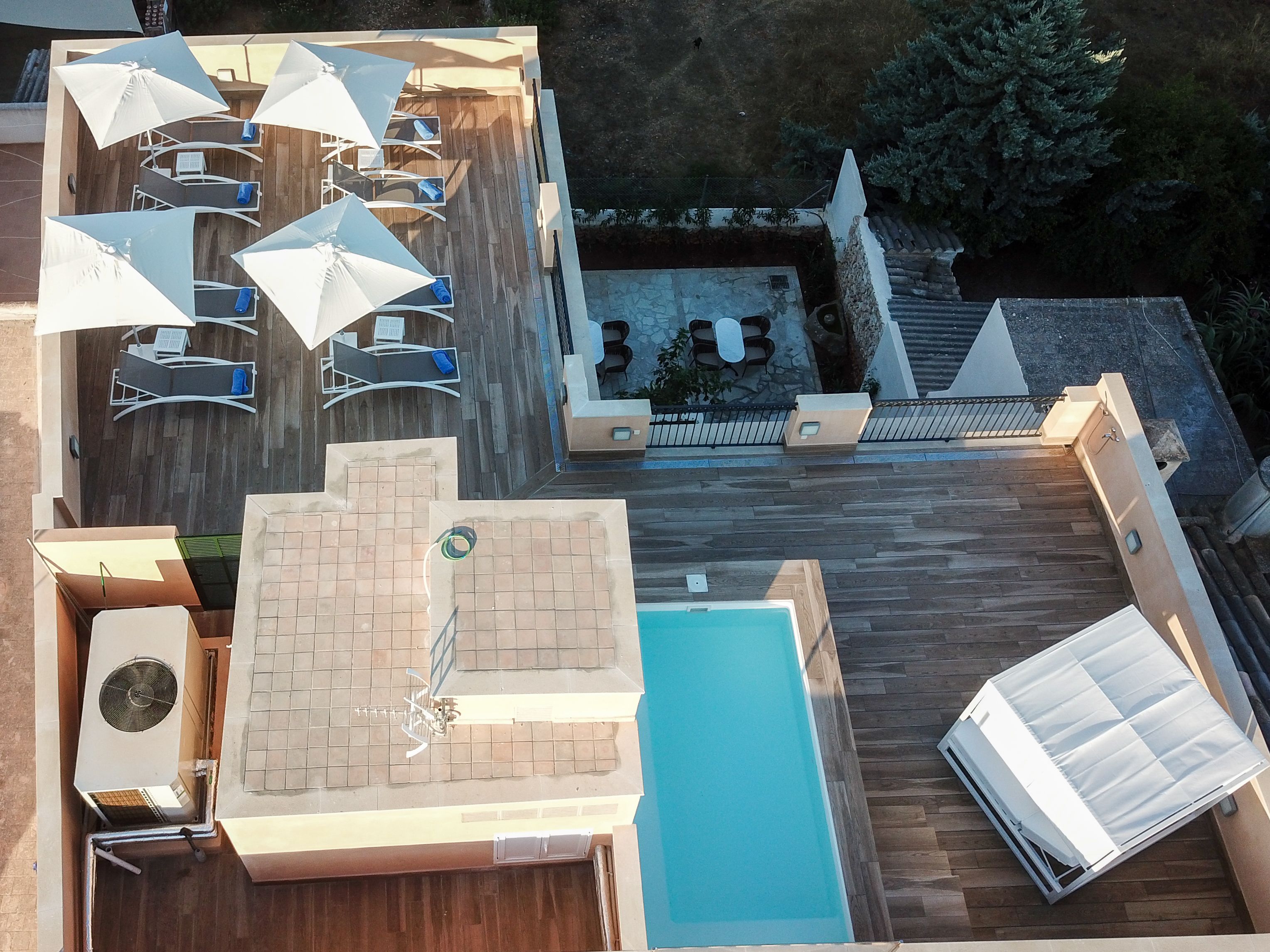 Un espace extérieur avec une piscine, des chaises longues et des parasols, un petit coin salon et un escalier menant à un niveau supérieur.