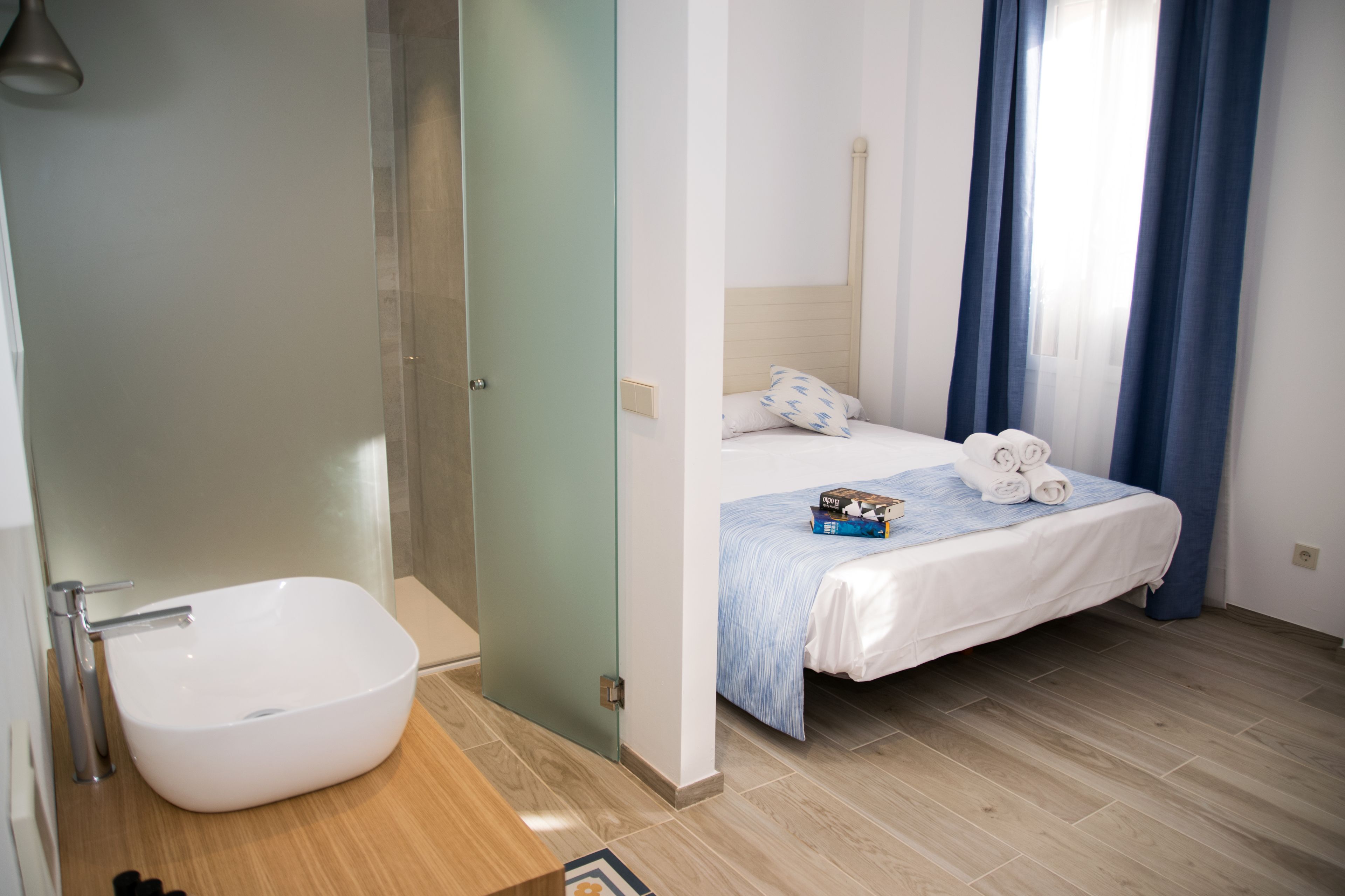 Un baño moderno con una bañera independiente, una zona de ducha y una cama con cubrecama a rayas azules y toallas enrolladas.
