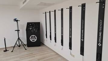 A room with a wall-mounted bike rack holding several bicycles, a tripod stand, and a black cabinet with a cycling logo.