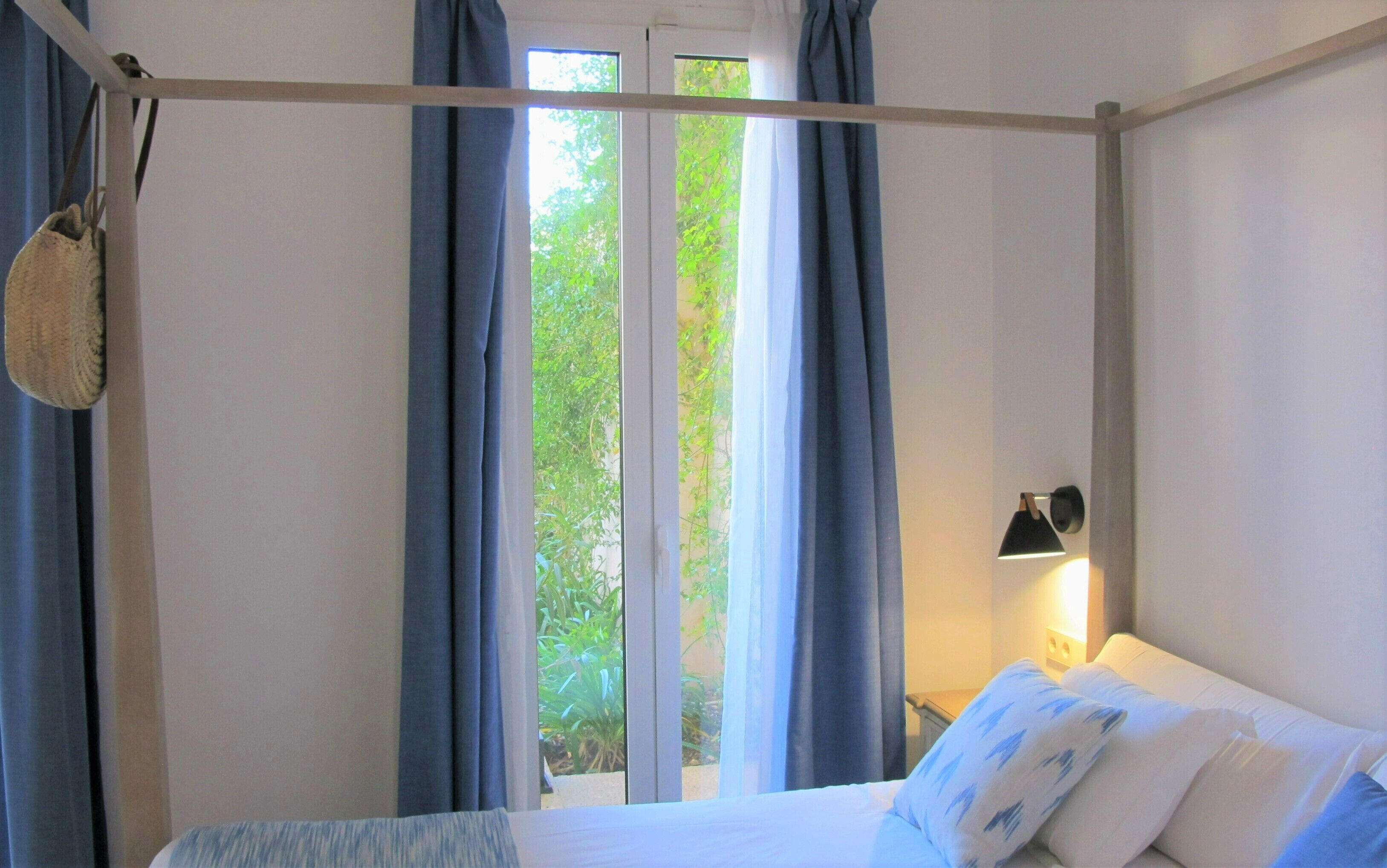 Ein Schlafzimmer mit Himmelsbett, Nachttischlampe und Blick auf Grün.