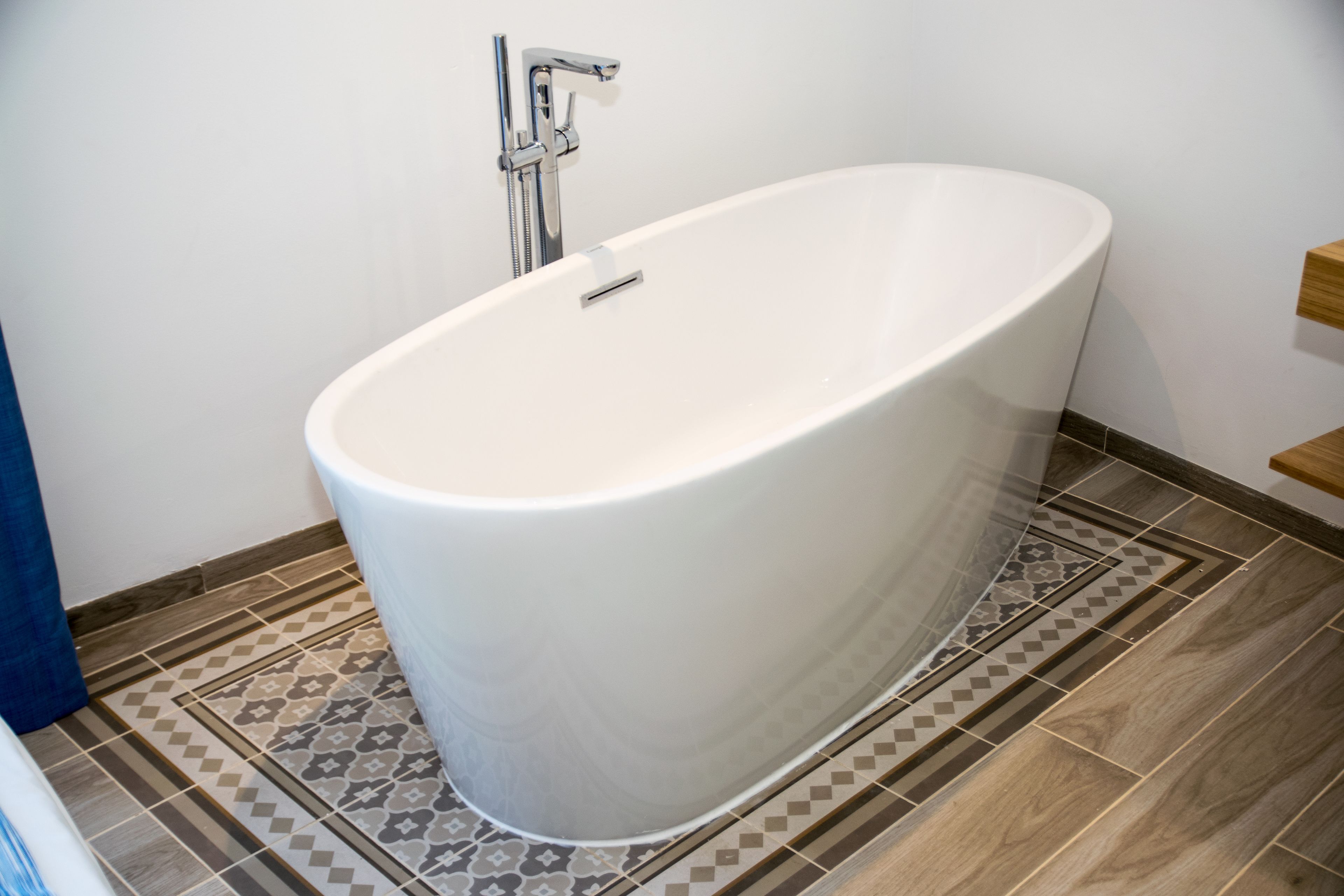 Un baño moderno con una bañera independiente, baldosas estampadas en el suelo y un estante de madera.