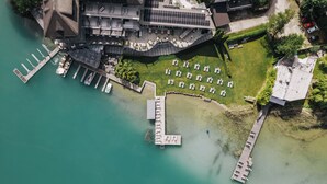 An aerial view of a waterfront hotel with a dock, outdoor seating area, and a building with a sloped roof. - Hotel Linde (Maria Woerth)