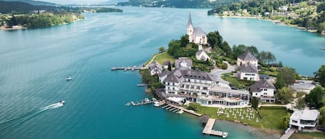Ett flygbildsbild av en fastighet vid en sjö, med ett kyrka, flera byggnader och båtar förtöjda vid en brygga.
