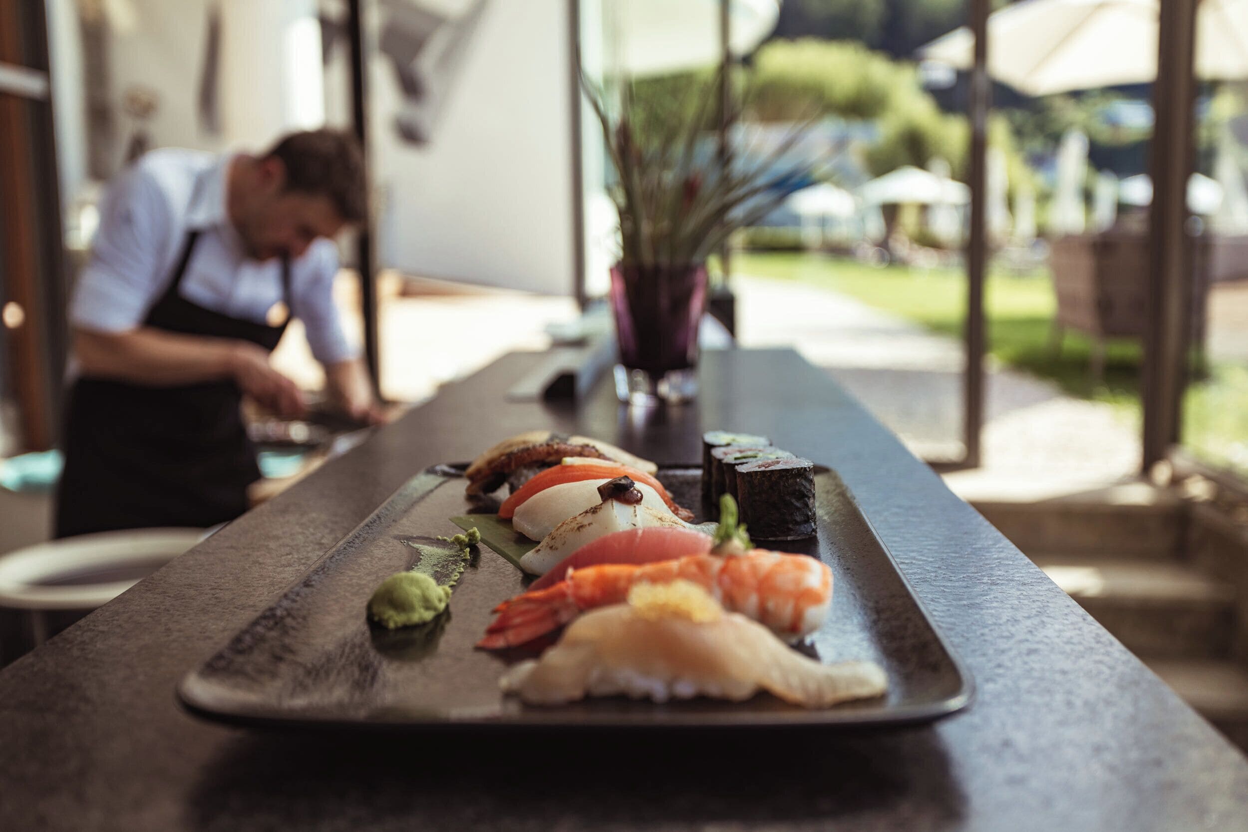 A sushi platter on a table with a chef in the background.