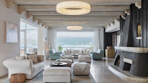 A spacious living room with a view of the lake, a fireplace, and a large window. - Hotel Linde (Maria Woerth)