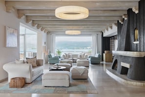 A spacious living room with a view of the lake, a fireplace, and a large window. - Hotel Linde (Maria Woerth)